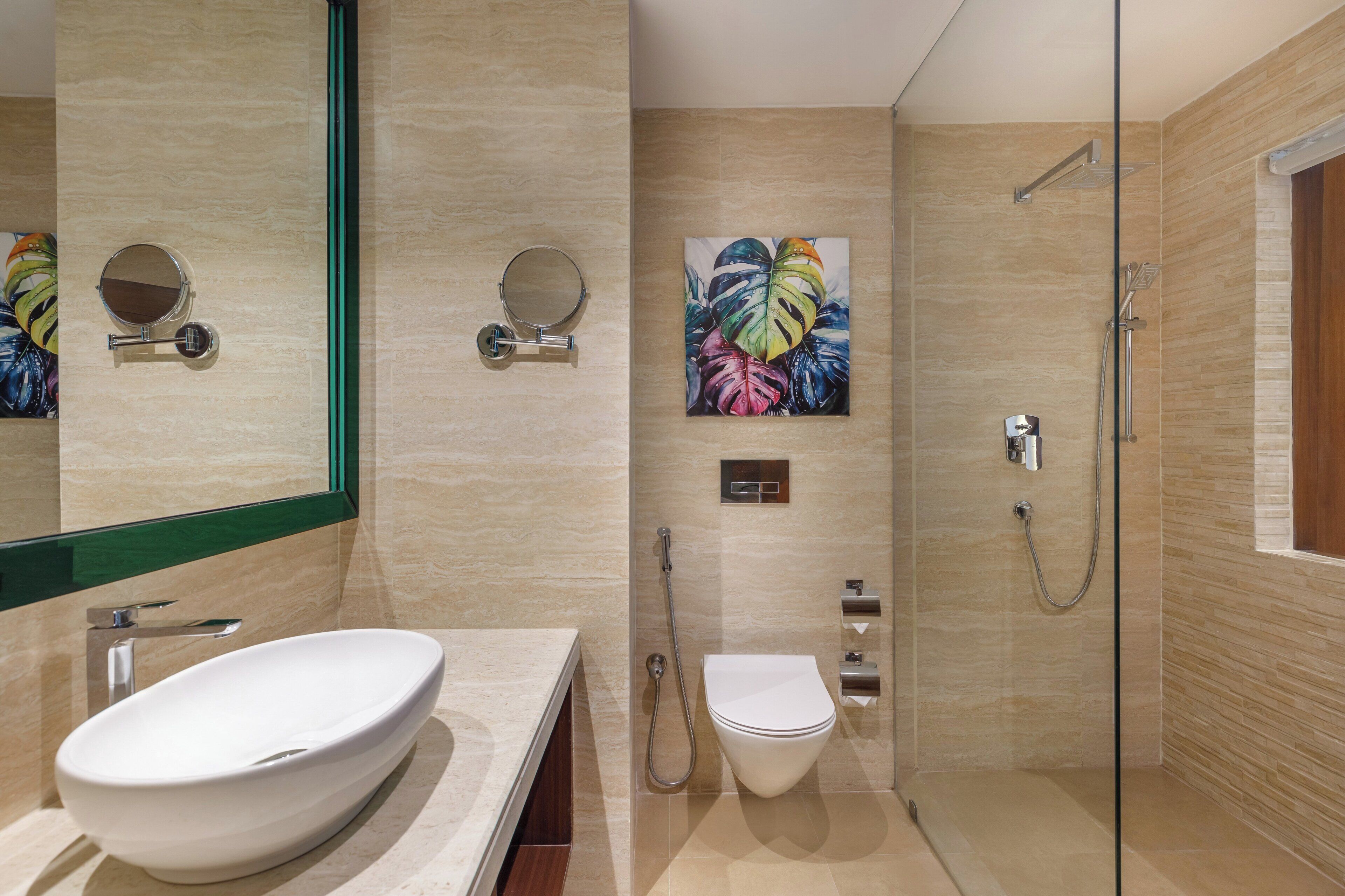 A modern bathroom with a large oval sink, a round mirror, a toilet, and a glass-enclosed shower area.