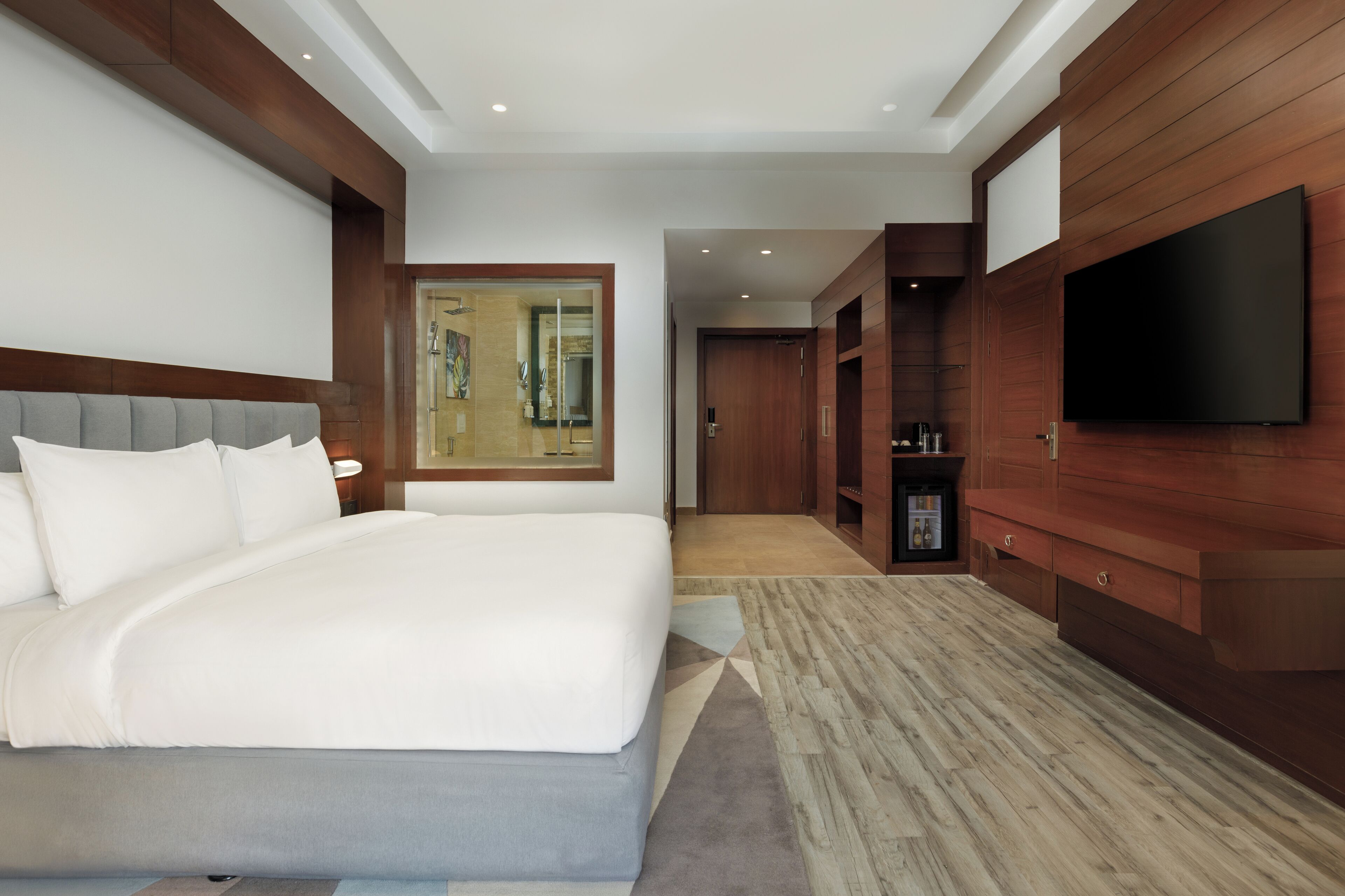Una habitación de hotel moderna con una cama grande, paneles de madera, un televisor de pantalla plana y un baño con cabina de ducha de vidrio.