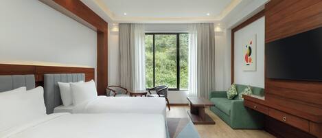 A hotel room with two beds, a TV, a sofa, a dining table, and a large window with curtains.