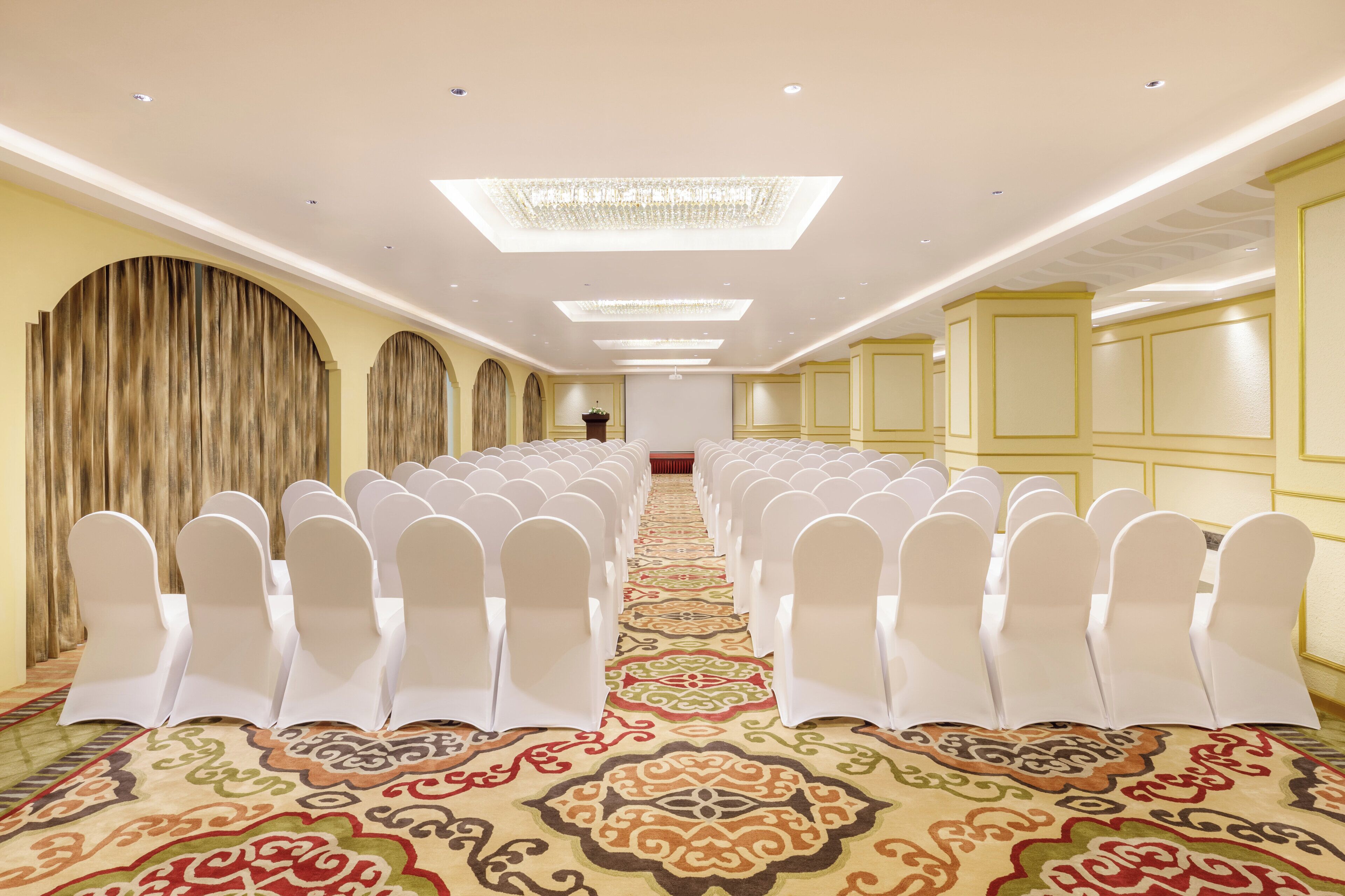 A conference room with rows of white chairs, a patterned carpet, and a chandelier.