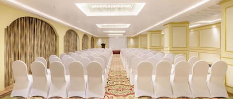 Un salón de conferencias con hileras de sillas blancas, una alfombra estampada y un candelabro.