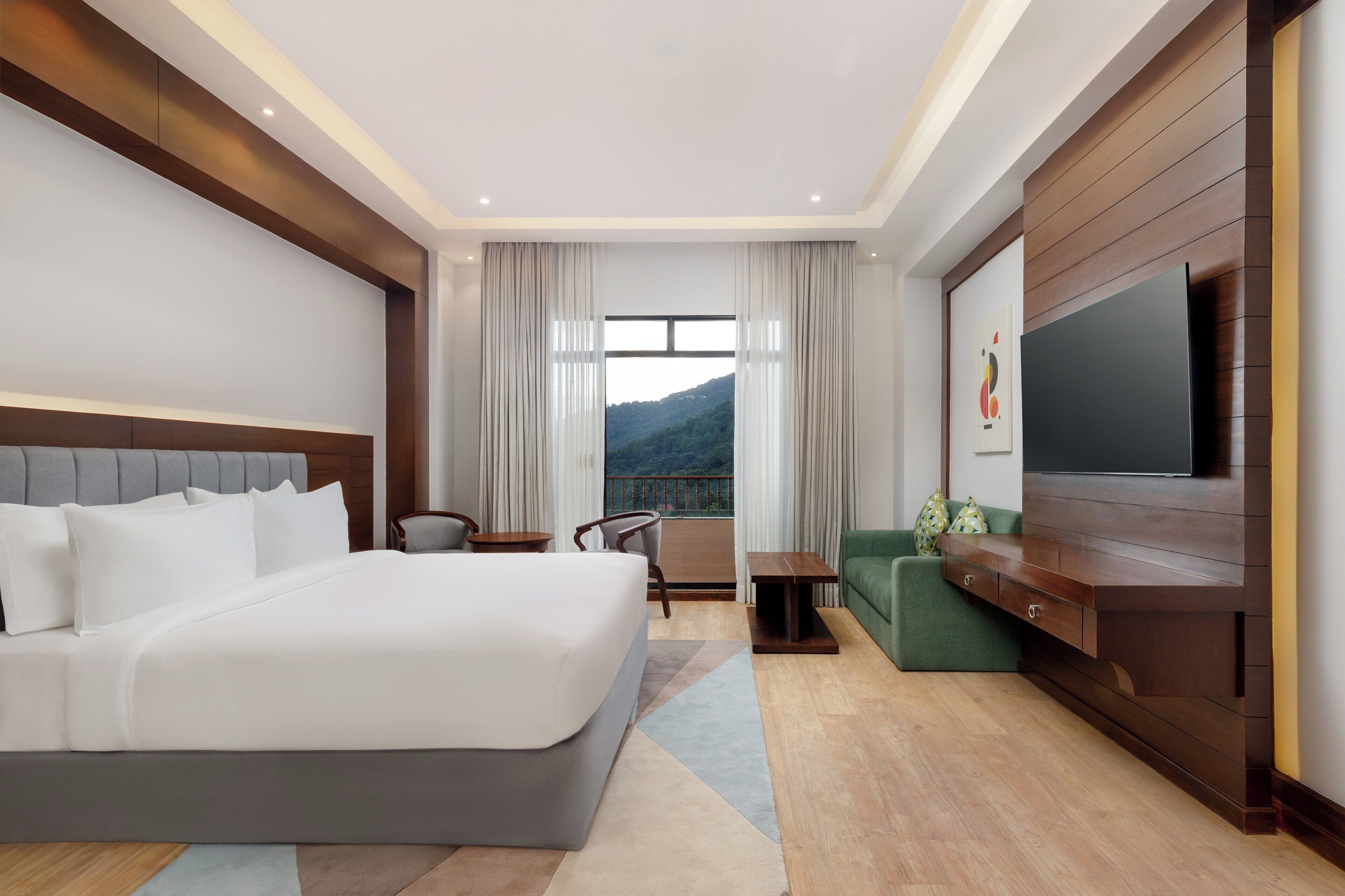 A modern hotel room with a large bed, a television, a sofa, and a view of a mountain.