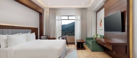A modern hotel room with a large bed, a television, a sofa, and a view of a mountain.