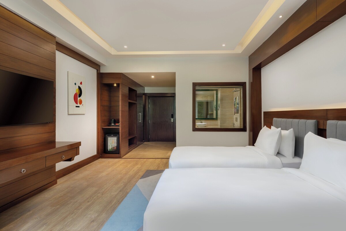 Une chambre d’hôtel moderne avec deux lits, une télévision, une armoire en bois et un tableau au mur.