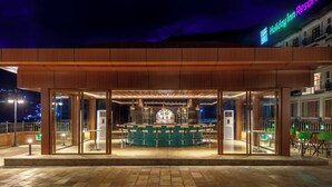 A bar area with a counter and stools, a large window, and a view of the city at night. - Holiday Inn Resort Kathmandu Budhanilkantha by IHG (Burhanilkantha)