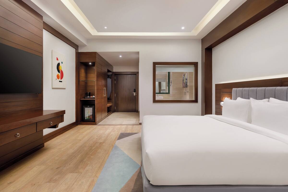 Una habitación de hotel moderna con una cama grande, muebles de madera, un televisor y un espejo.