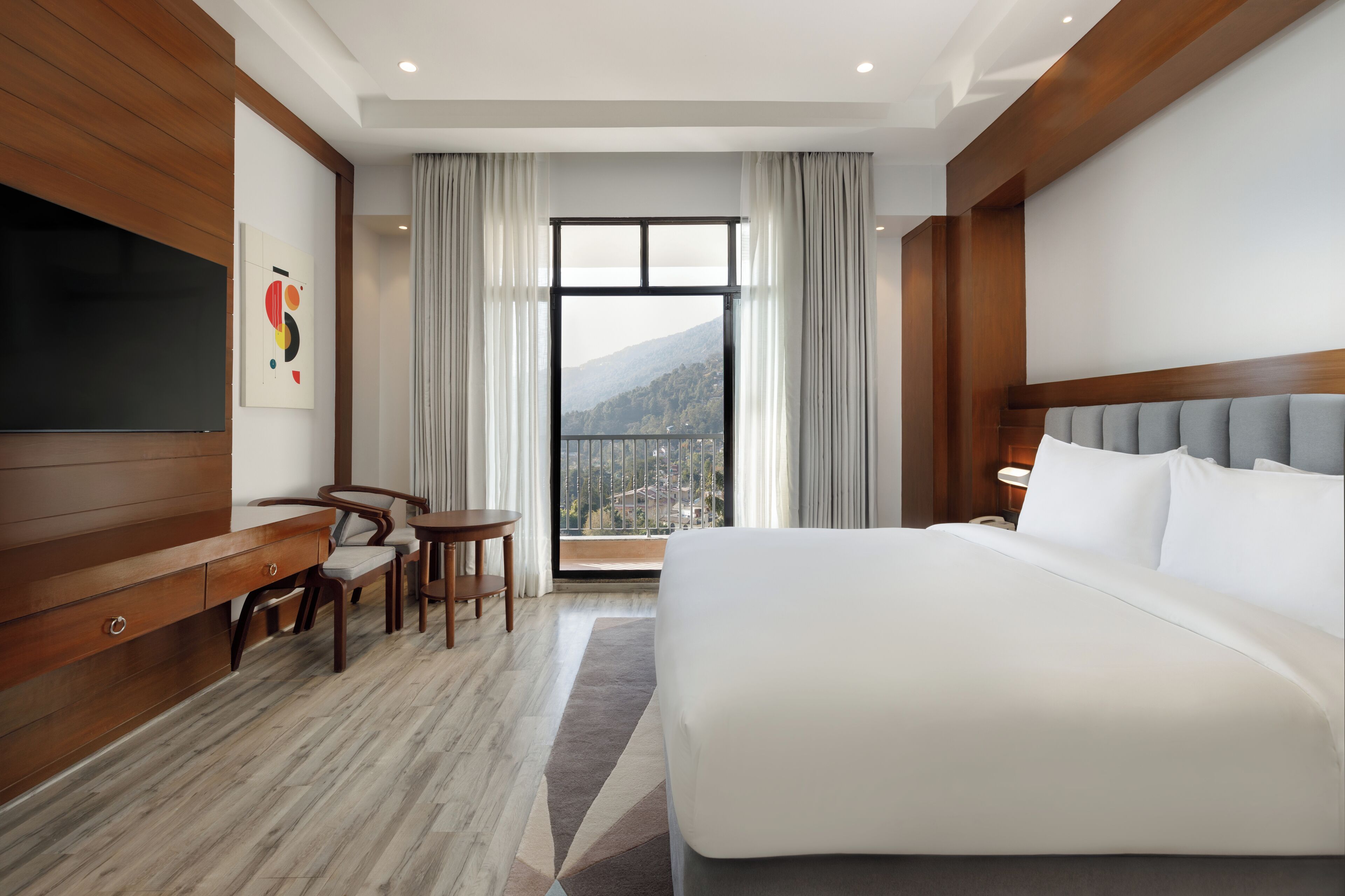 Ein Hotelzimmer mit einem großen Bett, einem Schreibtisch mit Stuhl, einem Fernseher und einem Fenster mit Stadtblick.