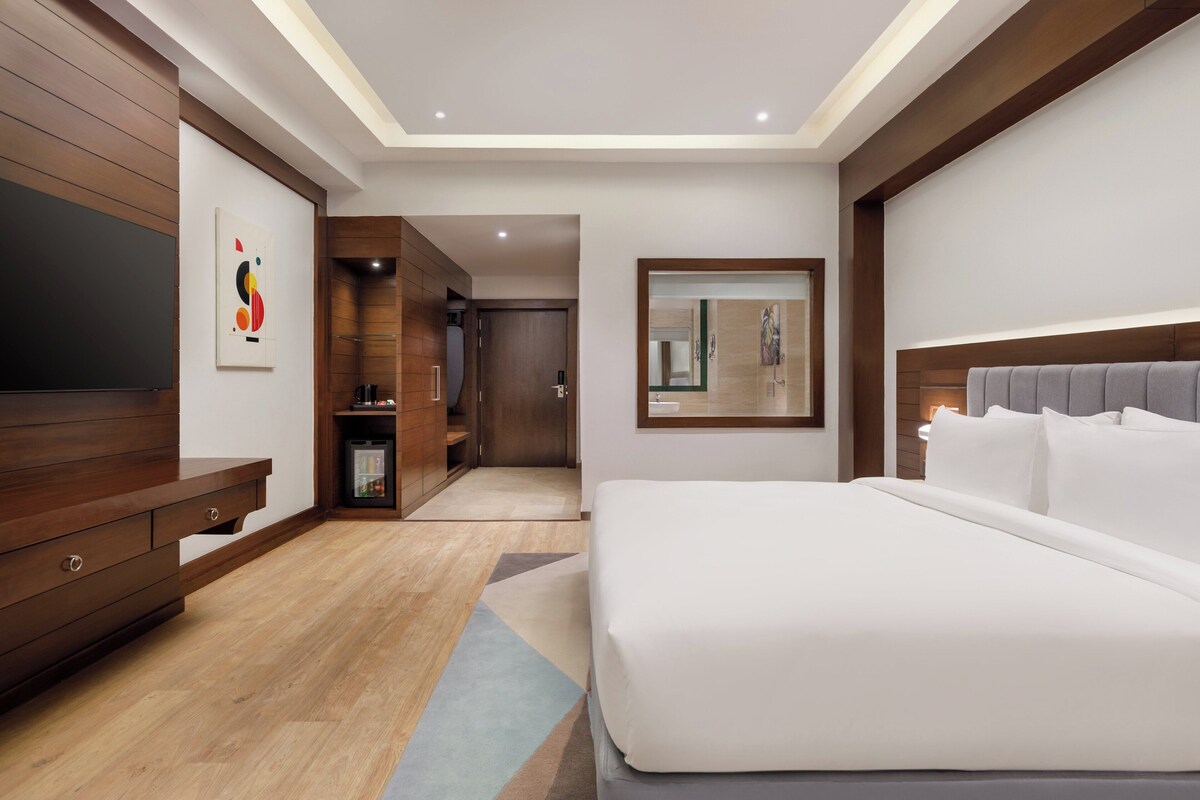 Une chambre d’hôtel moderne avec un grand lit, des meubles en bois, une télévision et un miroir.
