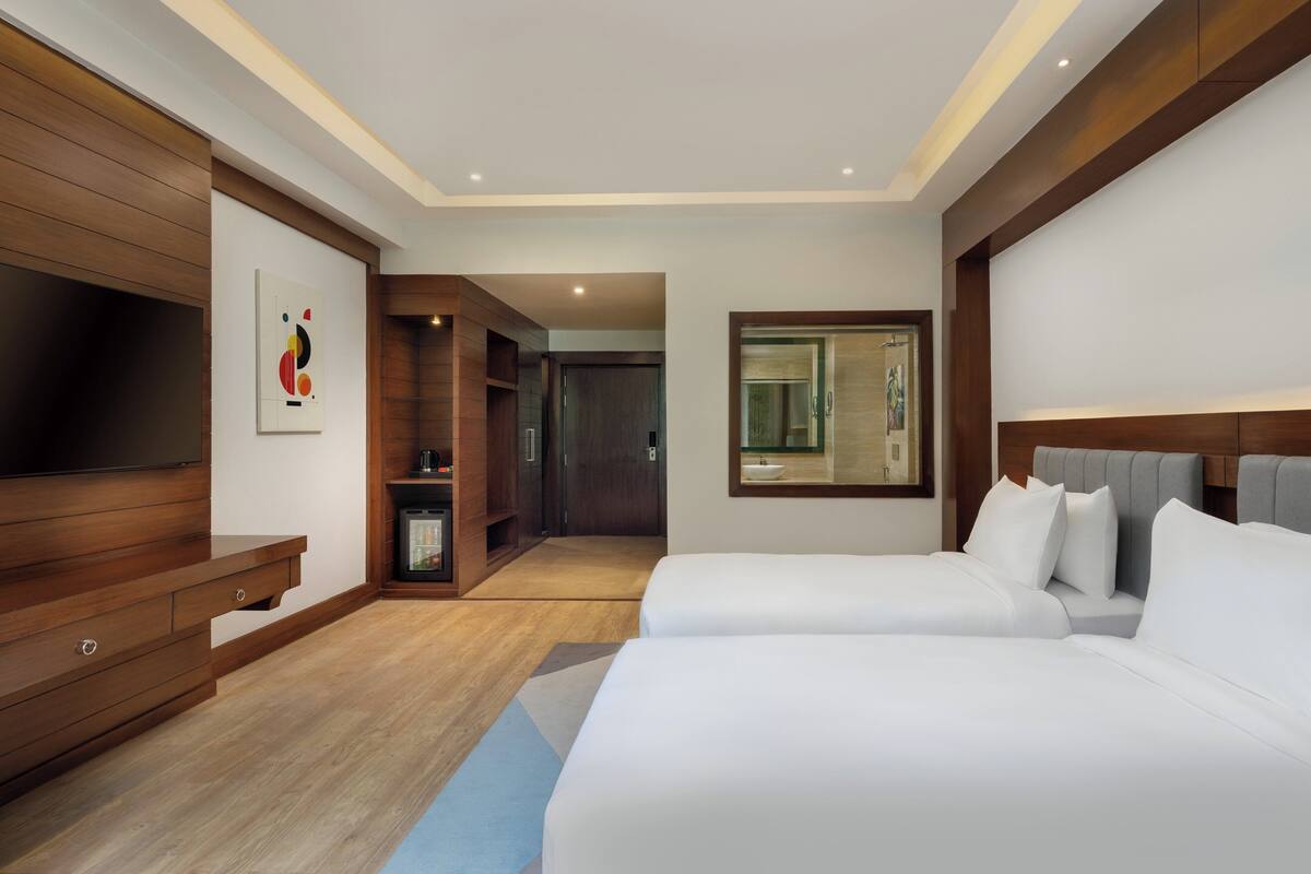 Una habitación de hotel moderna con dos camas, un televisor, un mueble de madera y un cuadro en la pared.