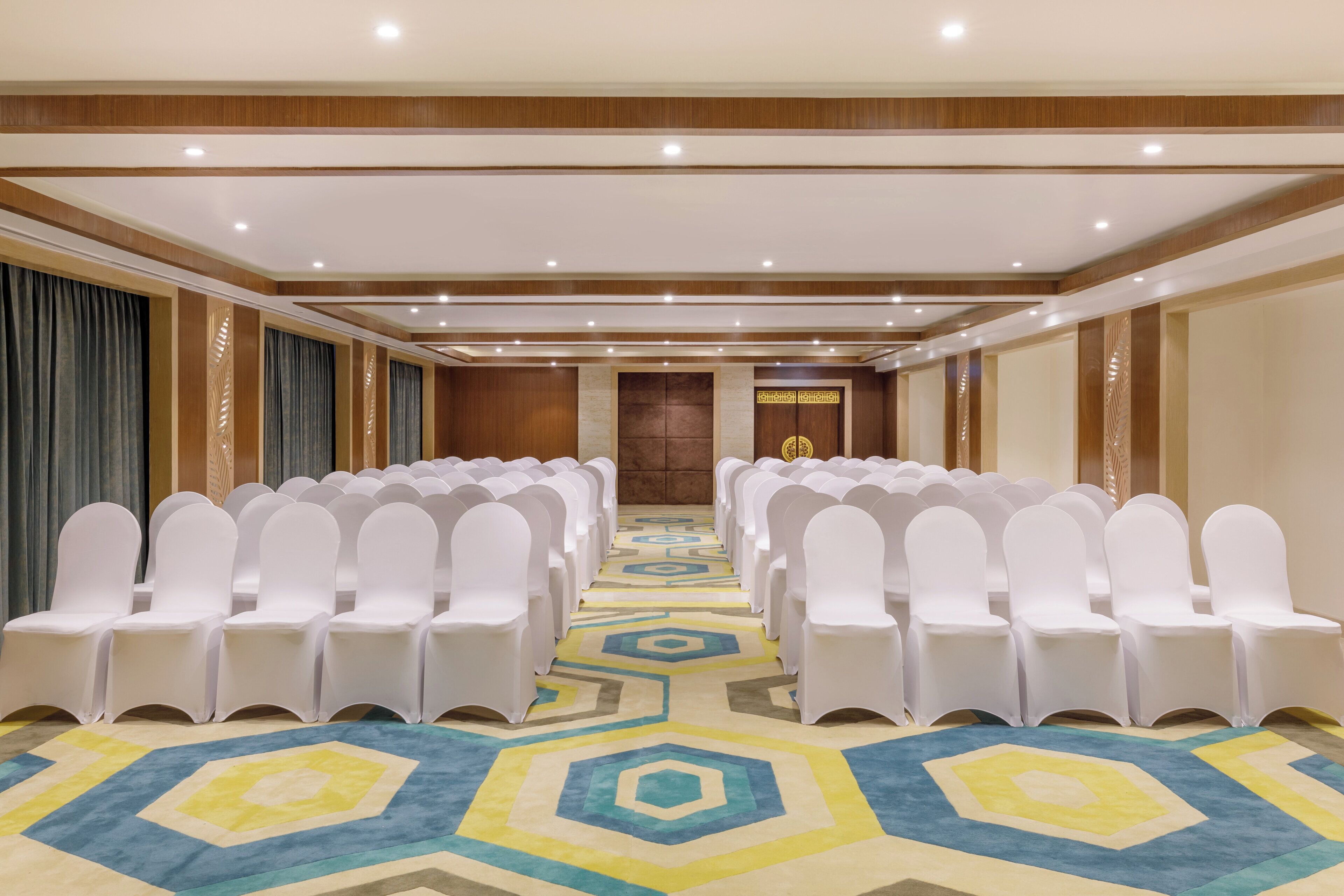 A conference room with rows of white chairs and a patterned carpet.