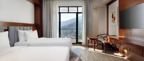 A hotel room with two beds, a TV, a desk, and a view of the mountains.