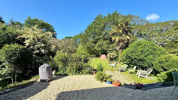 Un jardín con zona de grava, una parrilla cubierta y mobiliario de exterior.