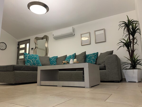 A living room with a grey sofa, teal and grey cushions, a white coffee table, and a potted plant.