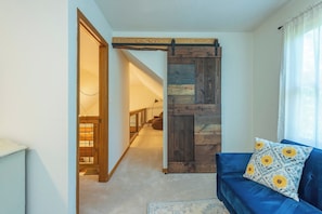 A room with a blue sofa, a wooden sliding door, and a view into another room. - Cozy Cabin in town with a View! Hot Tub+Grill+WiFi (Burnsville)