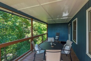 A covered outdoor seating area with a table and chairs, overlooking a forested area. - Cozy Cabin in town with a View! Hot Tub+Grill+WiFi (Burnsville)