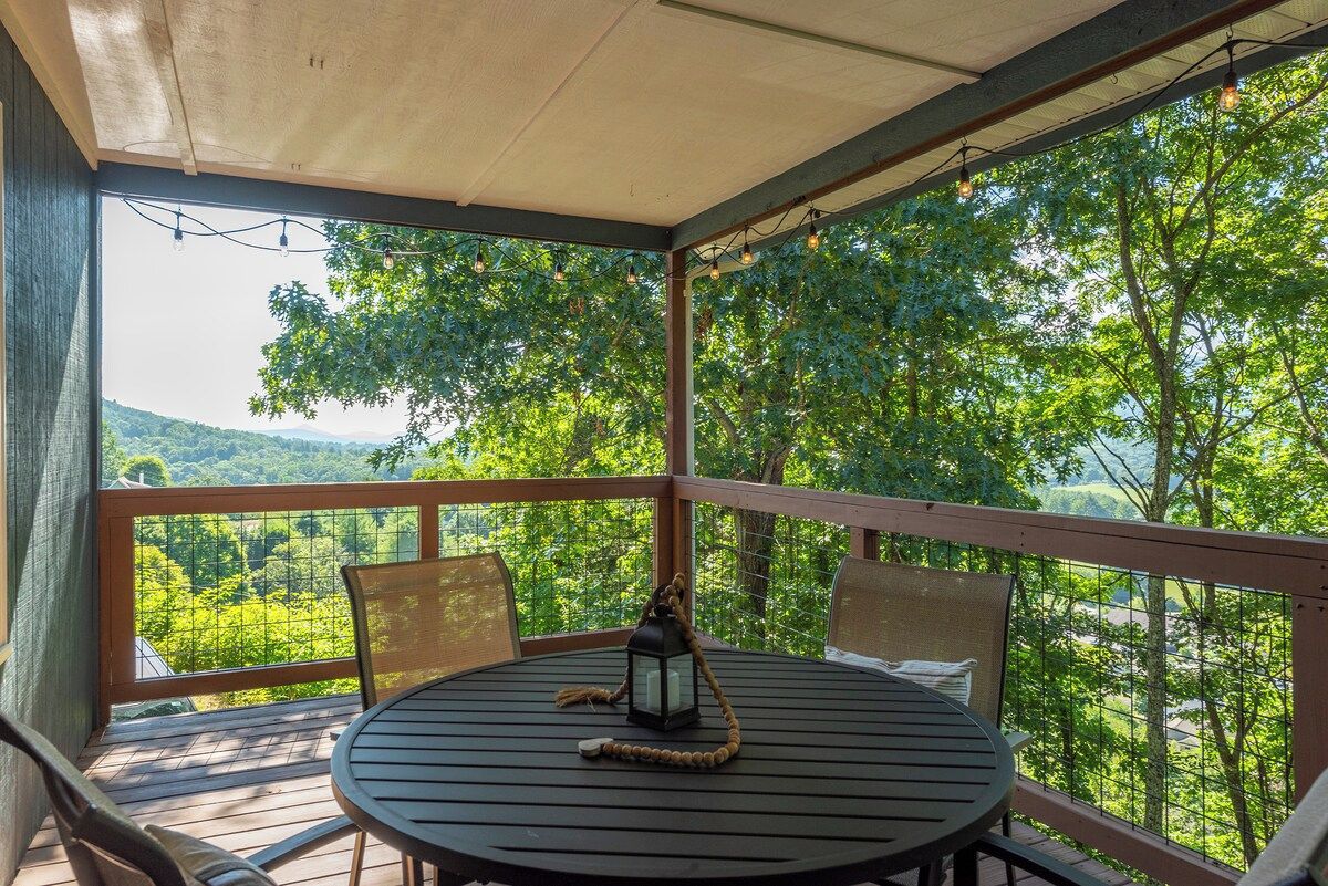 A covered outdoor seating area with a table and chairs, overlooking a lush green landscape.