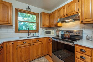 A kitchen with wooden cabinets, a microwave, an oven, and a window with a view of trees.