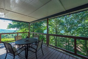 Eine überdachte Terrasse im Freien mit Tisch und Stühlen, mit Blick auf eine bewaldete Landschaft.