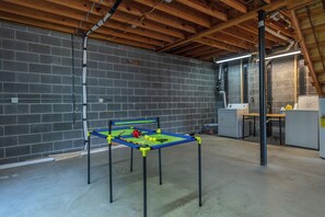 A room with a brick wall, a ping pong table, and a kitchen area.
