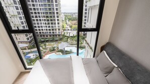 A high-rise hotel room with a large window overlooking a swimming pool and a landscaped courtyard. - Yumy Homestay Grand Park City (Ho Chi Minh City)