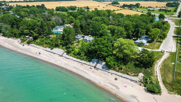 Vue aérienne d’une zone côtière avec une plage, des maisons et des éoliennes en arrière-plan.