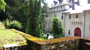 A historic building with a stone facade, a red door, and a courtyard surrounded by trees. - Apartment Near French Alps (Serrieres-en-Chautagne)