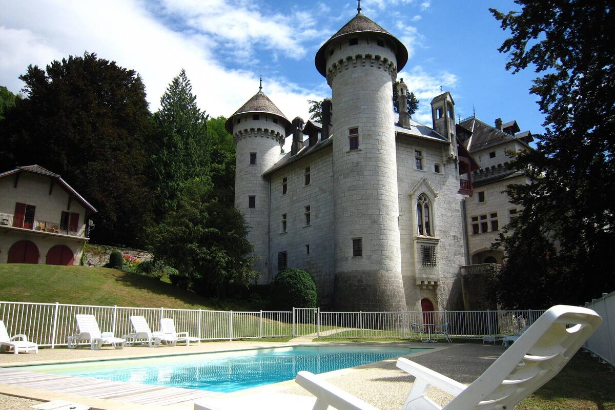 A castle with a swimming pool, white lounge chairs, and a white fence.