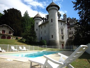 Un château doté d’une piscine, de chaises longues blanches et d’une clôture blanche.