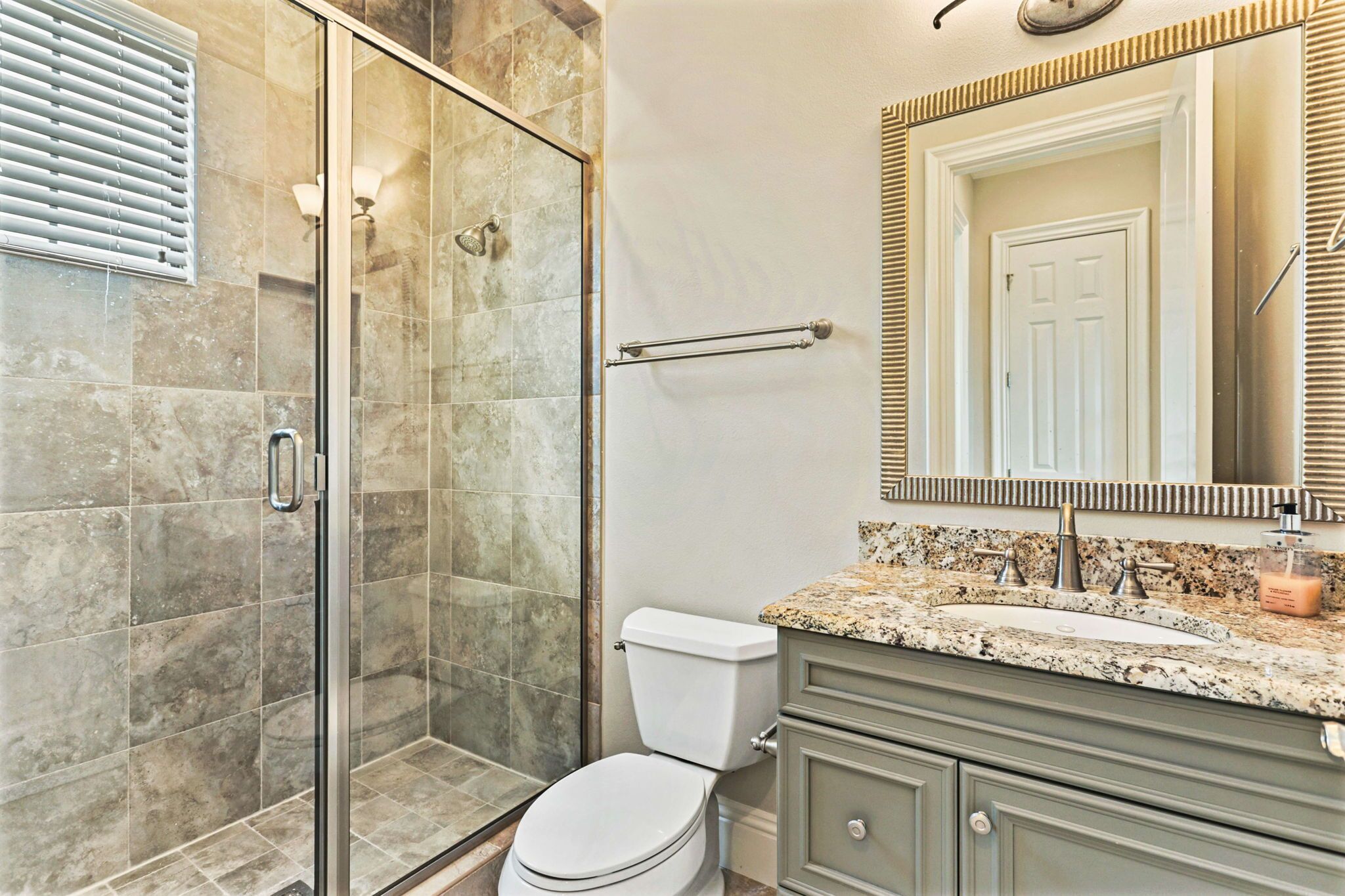 A bathroom with a glass shower enclosure, a toilet, a vanity with a sink, and a mirror with a decorative frame.