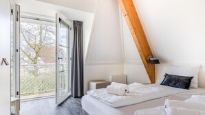 A bedroom with two beds, a large window, and a wooden ceiling beam. - Villa in Banjaard Near Sandy North Sea Beach (Kamperland)