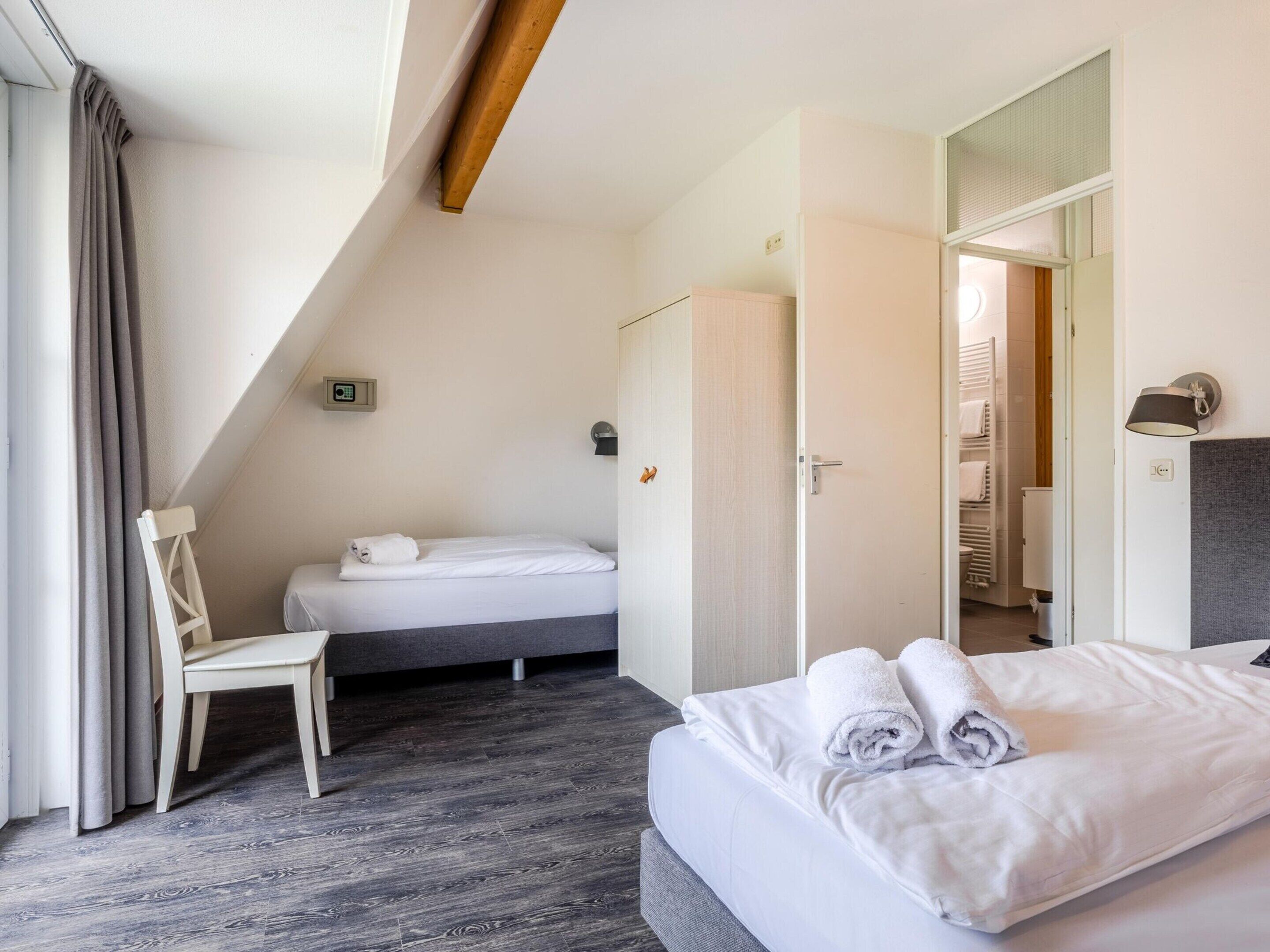 A hotel room with a bed, a chair, a wardrobe, and a bathroom visible through an open door.