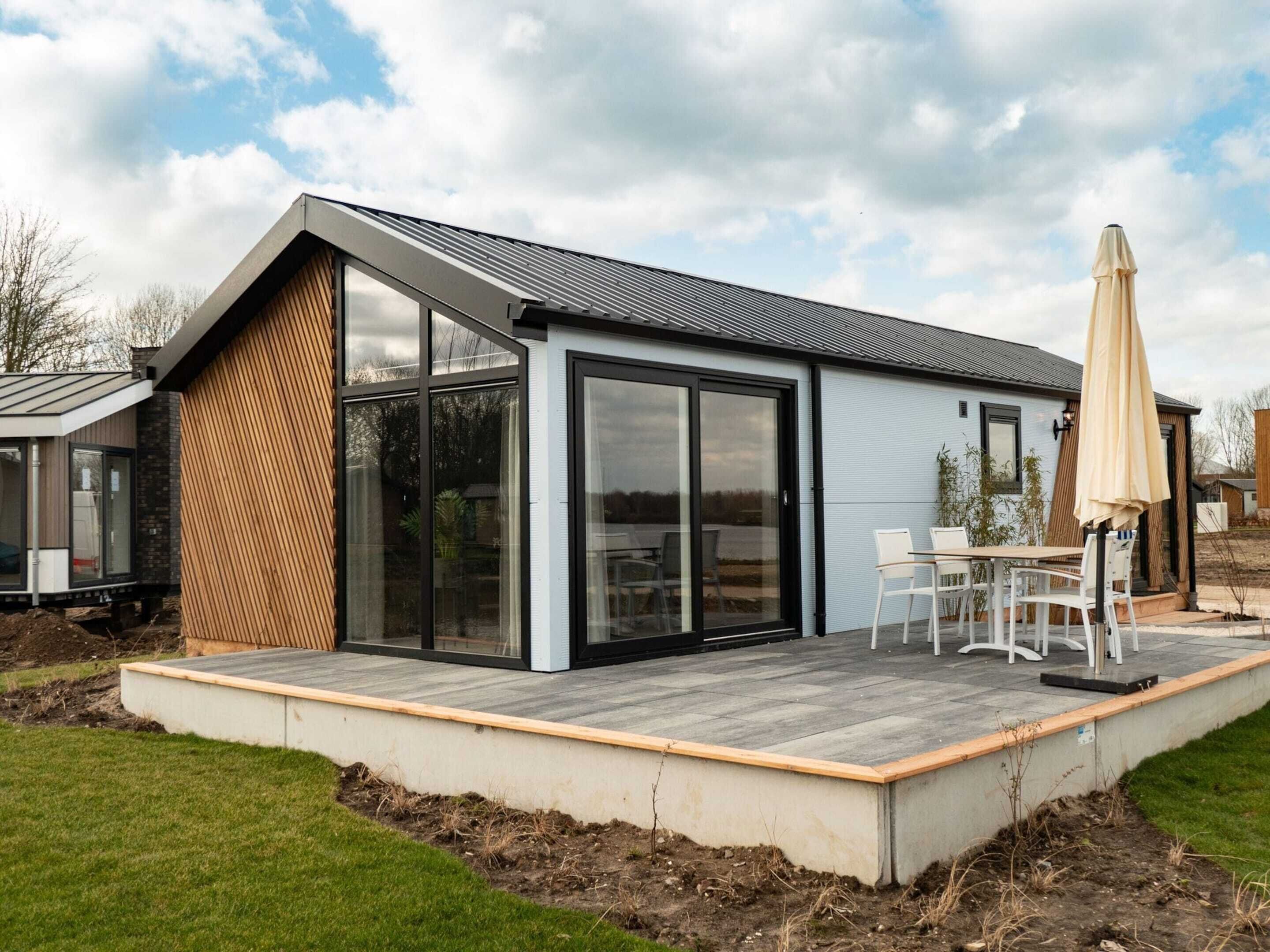 A modern house with a large glass door, a deck with outdoor furniture, and a clear sky.