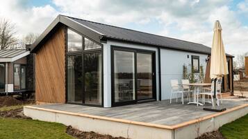 A modern house with a large glass door, a deck with outdoor furniture, and a clear sky.