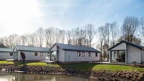 Uma fileira de casas móveis modernas, térreas, com janelas amplas e telhado plano, localizada ao lado de uma superfície aquática calma que reflete as construções.