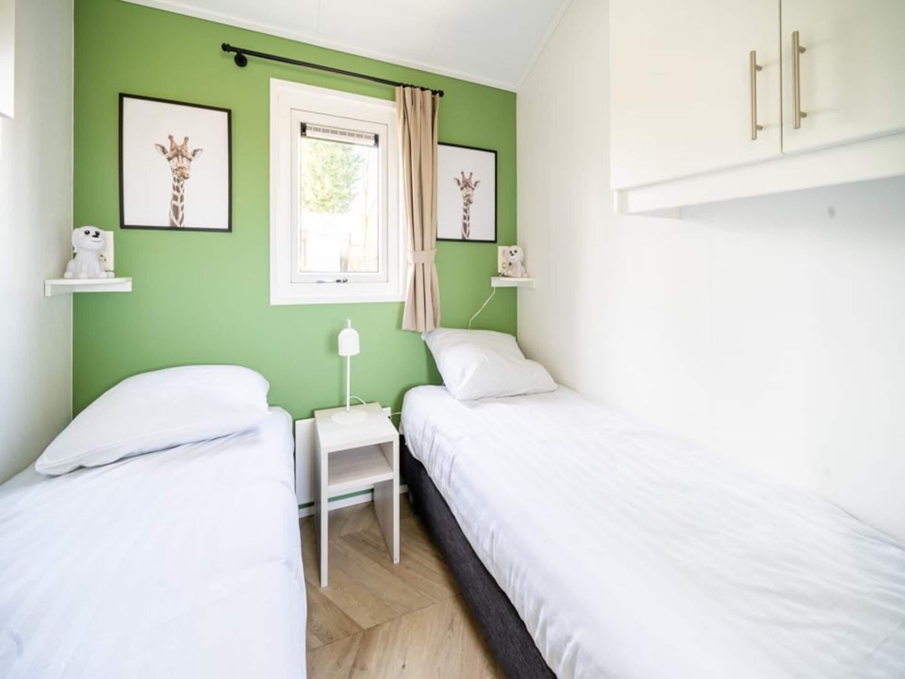 A bedroom with two beds, a window with curtains, a bedside table, and wall-mounted shelves with decorative items.