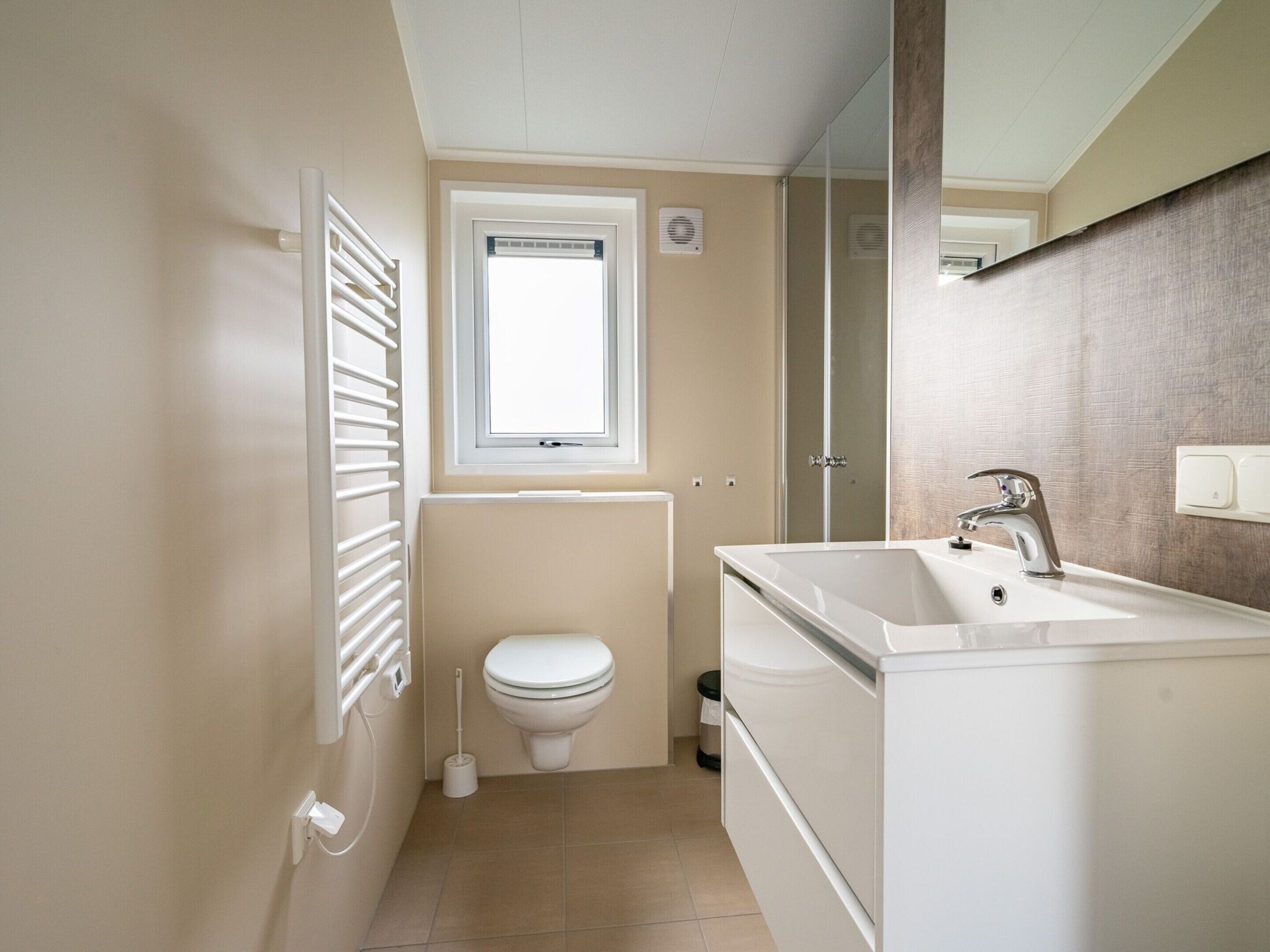 Een badkamer met toilet, raam, wastafel en spiegel.