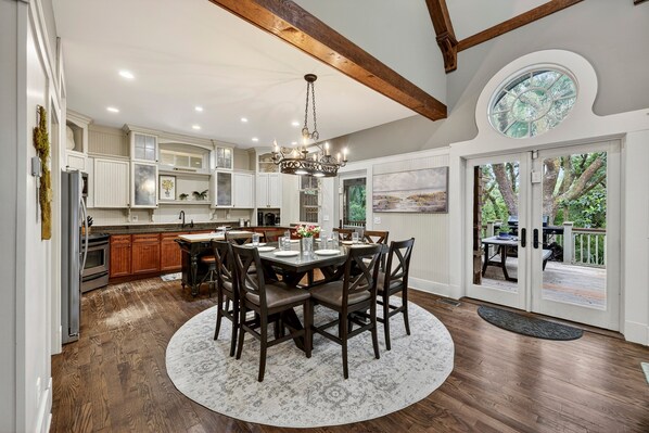 A spacious kitchen with white cabinetry, a dining area with a round table, and a view of the outdoors through large glass doors.