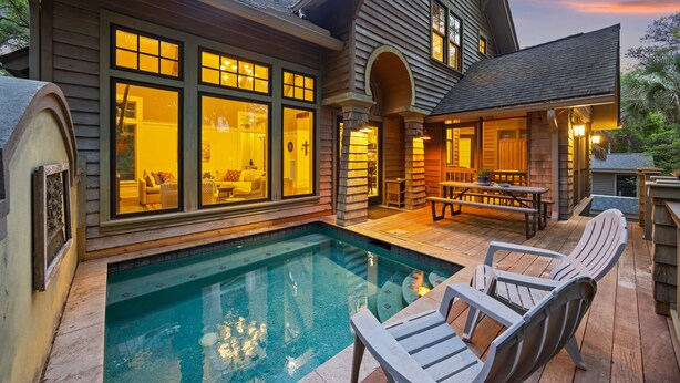 Ett hus med en swimmingpool, utomhusmöbler och stora fönster.