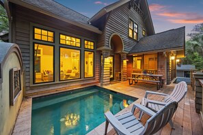 Une maison avec une piscine, un espace salon extérieur et une grande fenêtre donnant sur la piscine.