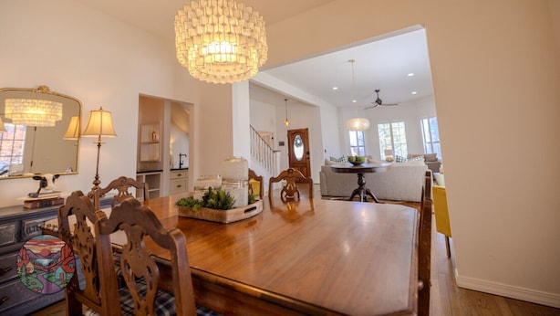 A spacious dining area with a large wooden table, a chandelier, and a view into a kitchen and living area.