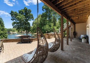 Une terrasse couverte avec des fauteuils en osier, une table en pierre et une vue sur un lac.