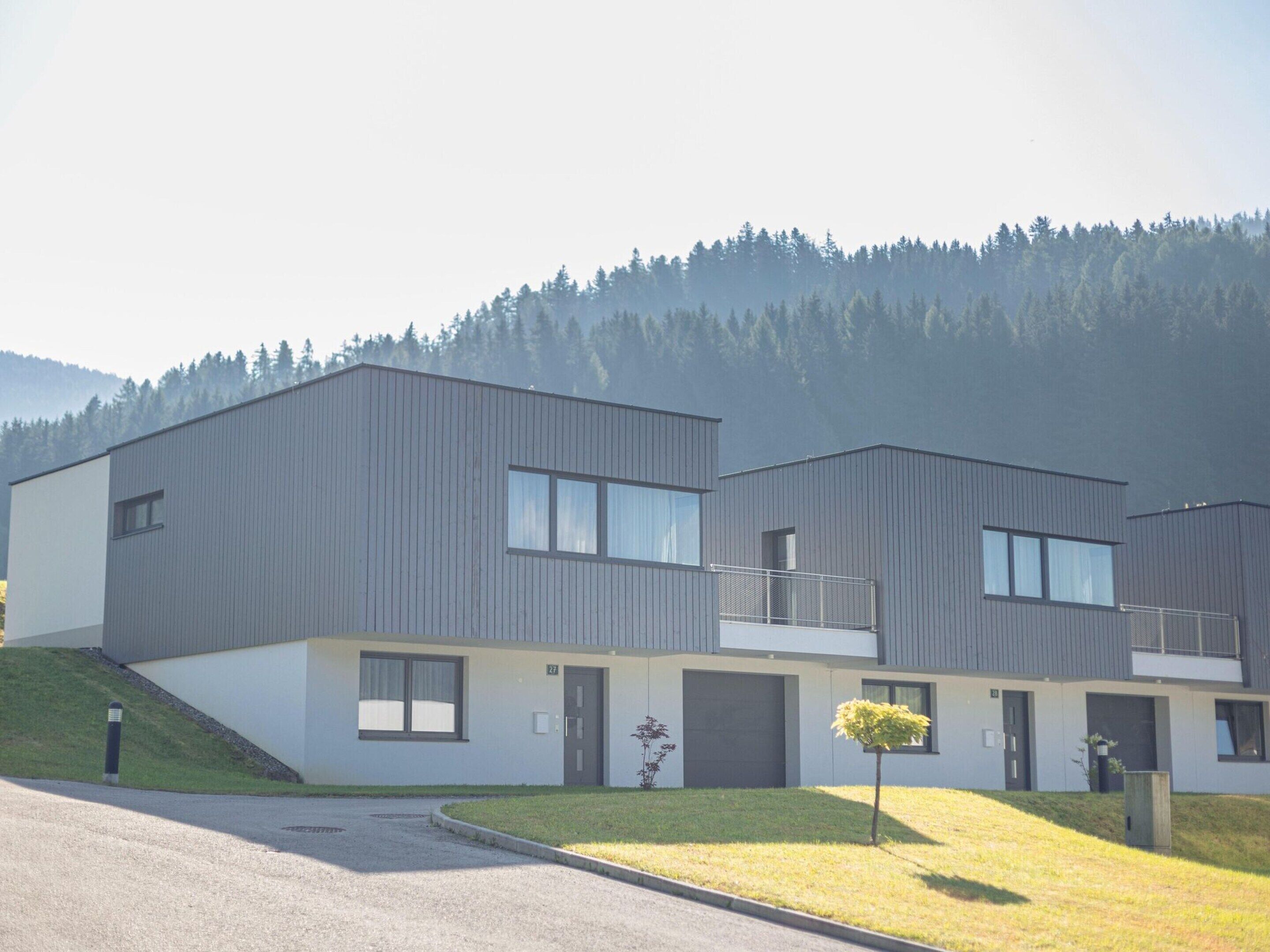 A modern two-story building with a flat roof, large windows, and a small balcony.