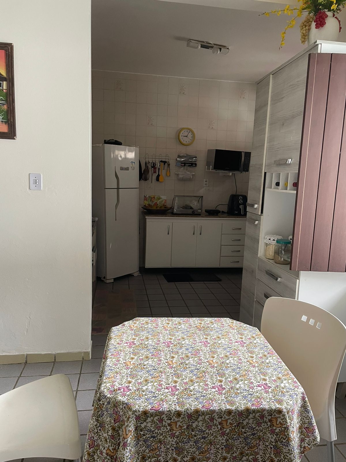 Uma cozinha compacta com geladeira, micro-ondas e um relógio na parede.