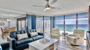 A modern living room with a blue sofa, beige armchairs, and a white coffee table. - Sailor's Delight 🌊 Deluxe 2-BR Condo @ Edgewater Beach & Golf Resort - Tower 1 (Panama City Beach)