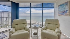 A room with a large window overlooking a beach, two beige armchairs, and a small round table. - Sailor's Delight 🌊 Deluxe 2-BR Condo @ Edgewater Beach & Golf Resort - Tower 1 (Panama City Beach)