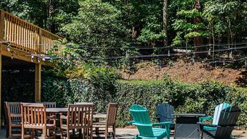 Une terrasse extérieure aménagée avec des meubles en bois et des fauteuils Adirondack, entourée d’une végétation luxuriante et d’arbres.