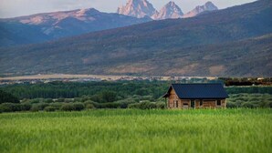 Een houten chalet in een grasveld, met een bergketen op de achtergrond.