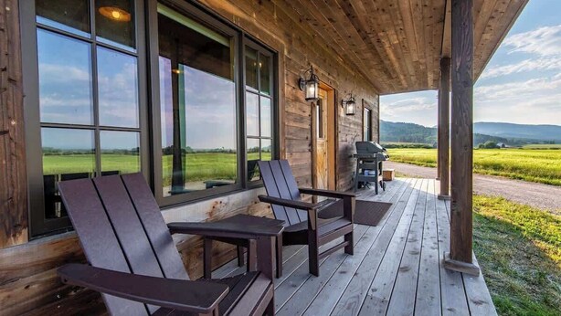 Een houten terras met twee Adirondack-stoelen en een tafel, met uitzicht op een groen landschap.