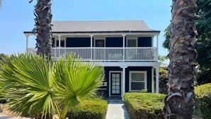 A two-story house with a balcony, a pathway leading to the front door, and a palm tree in the foreground.