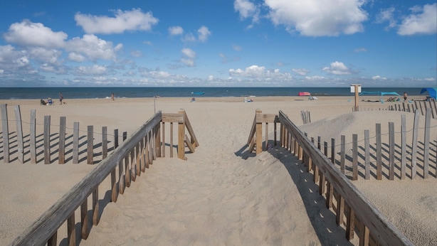 A beach with wooden walkways leading to the water, a lifeguard tower, and beach umbrellas. - 7081- Sea View - Rodanthe Condo | Coastal Beach Escape (Rodanthe)